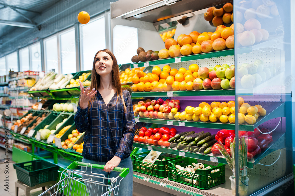 Shopping woman looking at the shelves in the supermarket with shopping cart.  Portrait of a young girl in a market store at fruits and vegetables section.