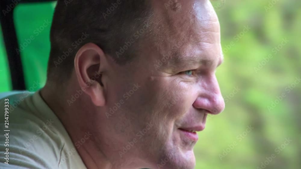 A man smiles and looks out of the window. A vehicle is driving on the road. The day is really nice. A man smiles and looks out of the window. A vehicle is driving on the road. The day is really nice.