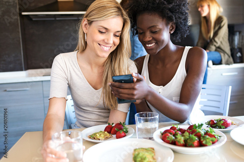 Young women watching her mobile phone while having lunch with friends at home.