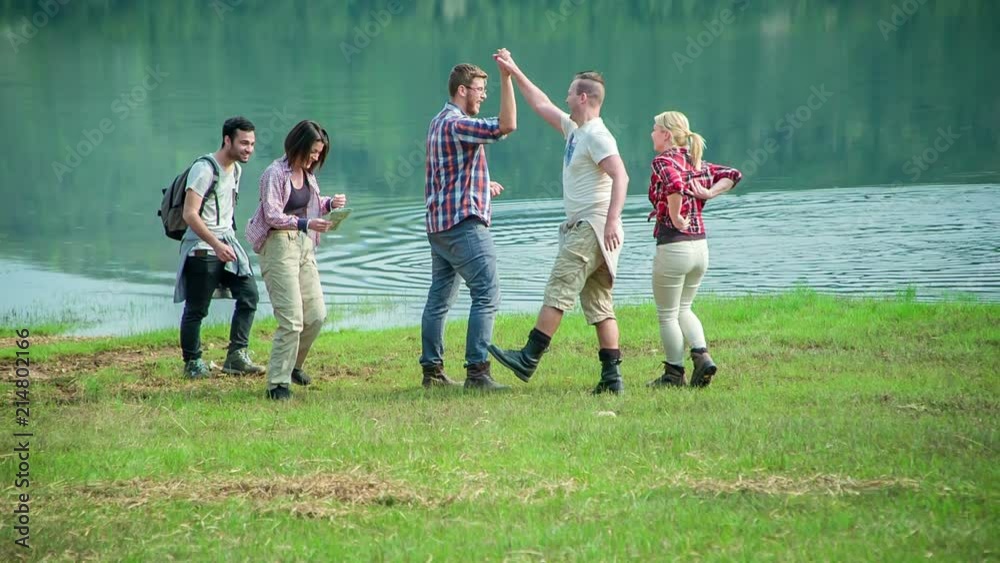 A group of young folks is really relaxed by the lake. They're laughing and giving each other a high five. A group of young folks is really relaxed by the lake. They're laughing and giving each other a high five.