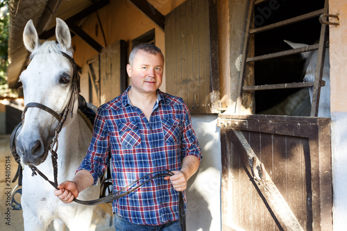 Positive male farmer standing  with white horse  at stable