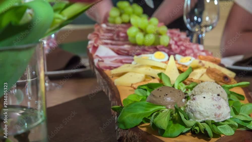 The waitress is putting a cold starter which consists of cheese, meat, grapes and eggs on the table in front of the guests. She brings the food on a wooden board. The waitress is putting a cold starter which consists of cheese, meat, grapes and eggs on the table in front of the guests. She brings the food on a wooden board.