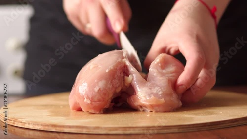 Female chef cuts raw chicken meat on a round wooden Board. High resolution. The view from the top. Cook chef hands woman cuts raw meat chicken breast on a wooden background photo