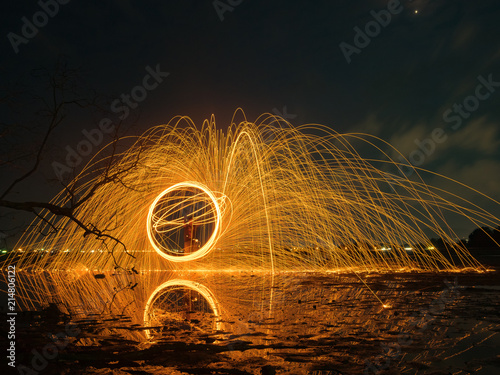 light lines of steel wool with long exposure, speed motion abstract background in the dark night with dry branch tree and reflection in water