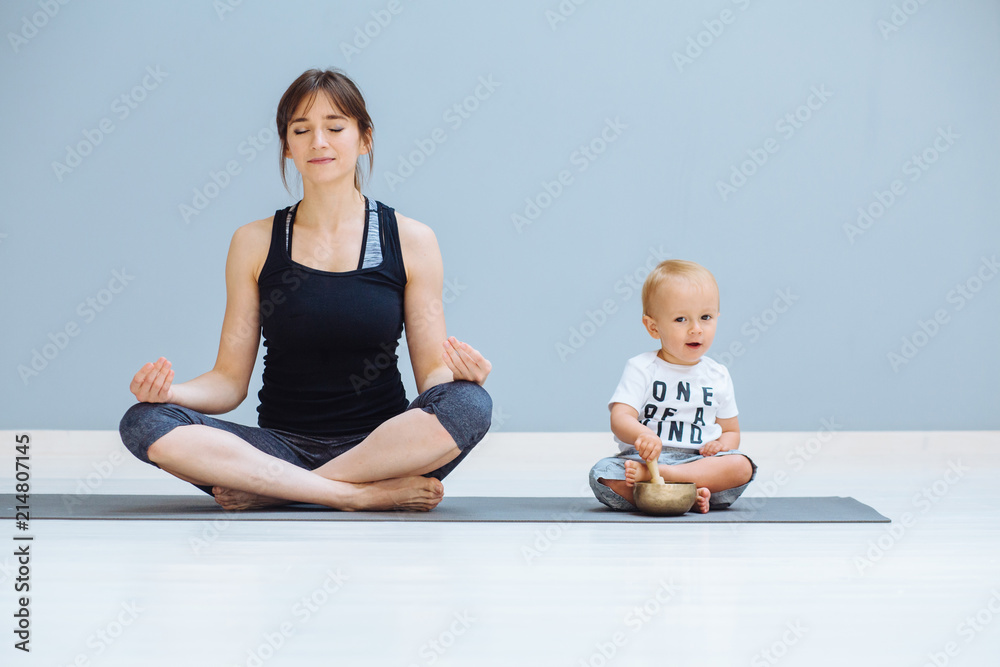 Cute toddler baby boy sitting in lotus pose with Tibetan singing bowl while  his mother meditating in a yoga on grey background, Yoga together,  motherhood, healthy lifestyle concept. Stock Photo | Adobe