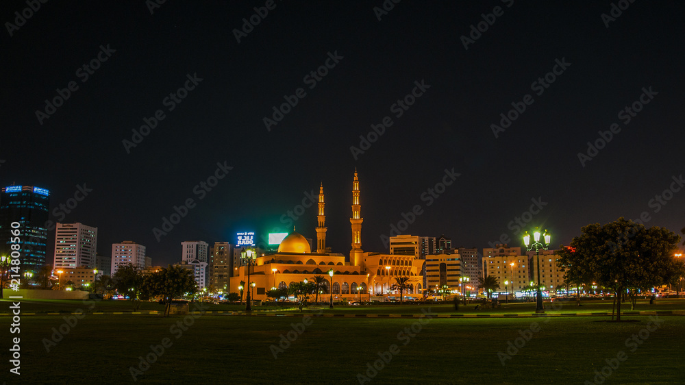 King Faisal mosque at nigh,the biggest mosque in Sharjah . People are resting near mosque in a park.