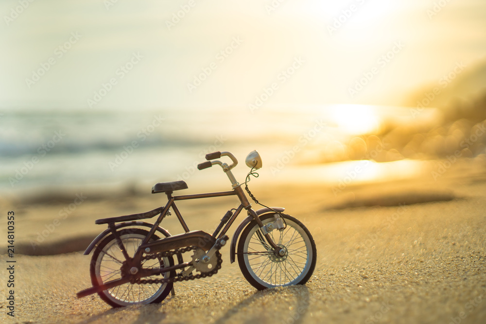Fototapeta premium bicycle transport toy on sand sea beach in the evening sunset sky , with yellow light beam