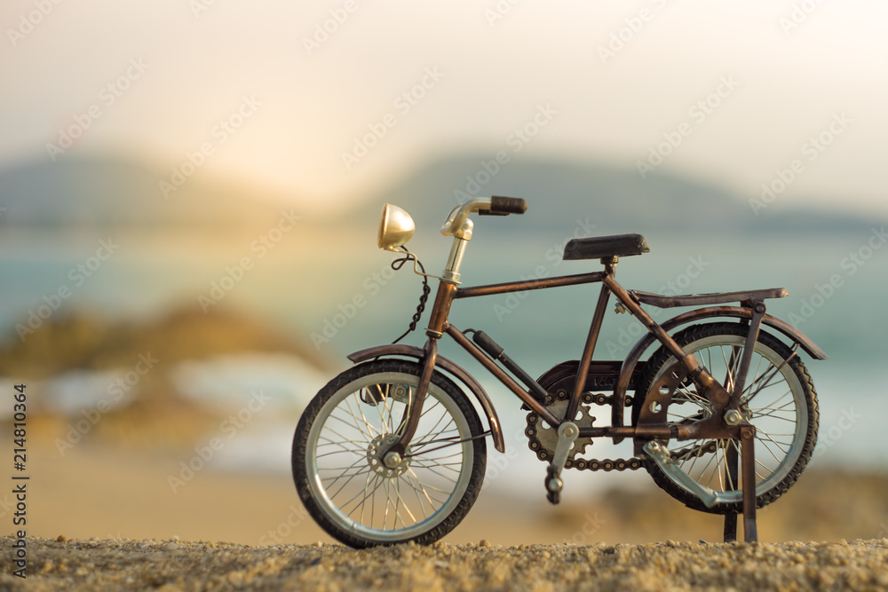 Obraz premium bicycle transport toy on sand sea beach in the evening sunset sky , with yellow light beam
