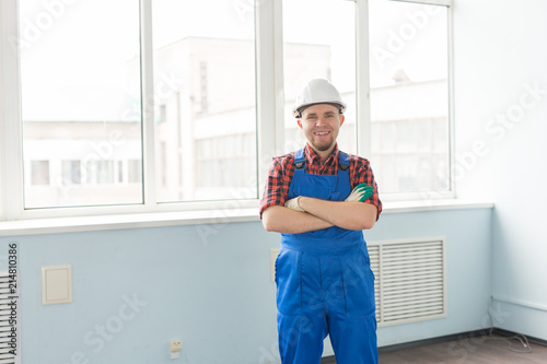 Happy caucasian male builder with crossed hands wearing white helmet in front of window