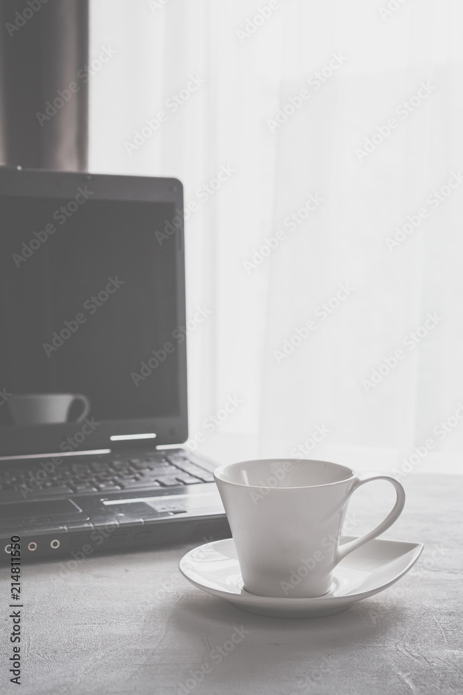 cup of coffee and a laptop on a table near a window in Scandinavian style minimalism in gray with a copy space