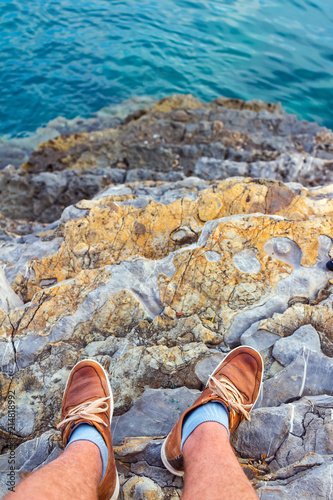 Male two legs in sneakers on high rock, view to the turquoise water in Adriatic sea at Montenegro