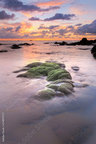 view of beautiful sunset sky at unknown beach in Sabah, Malaysia. Natural coastal rocks covered by green moss on the ground. soft focus due to long expose.