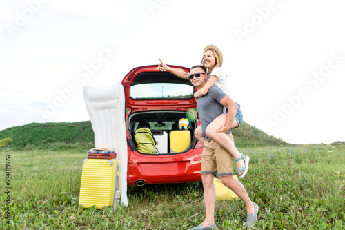 Cheerful couple having fun near the red car with travel suitcases, traveling around the world