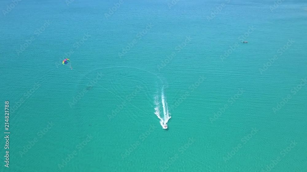 Parasail flying over blue sea pulled boat aerial view. Parasailing over blue sea drone view. Summer activity and extreme entertainment while resting on resort beach. Parasail flying over blue sea pulled boat aerial view. Parasailing over blue sea drone view. Summer activity and extreme entertainment while resting on resort beach.