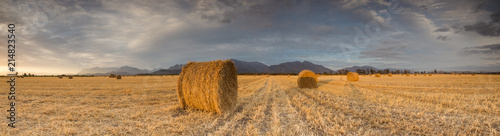 Panoramic views of a brilliant sunset over a meadow with big hay bales.