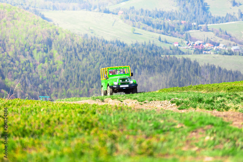 A green jeep car rises to the mountains along the road against the background of the beautiful Carpathian Mountains
