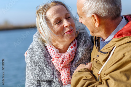 Portrait of happy senior couple embracing by the lake on sunny autumn day.