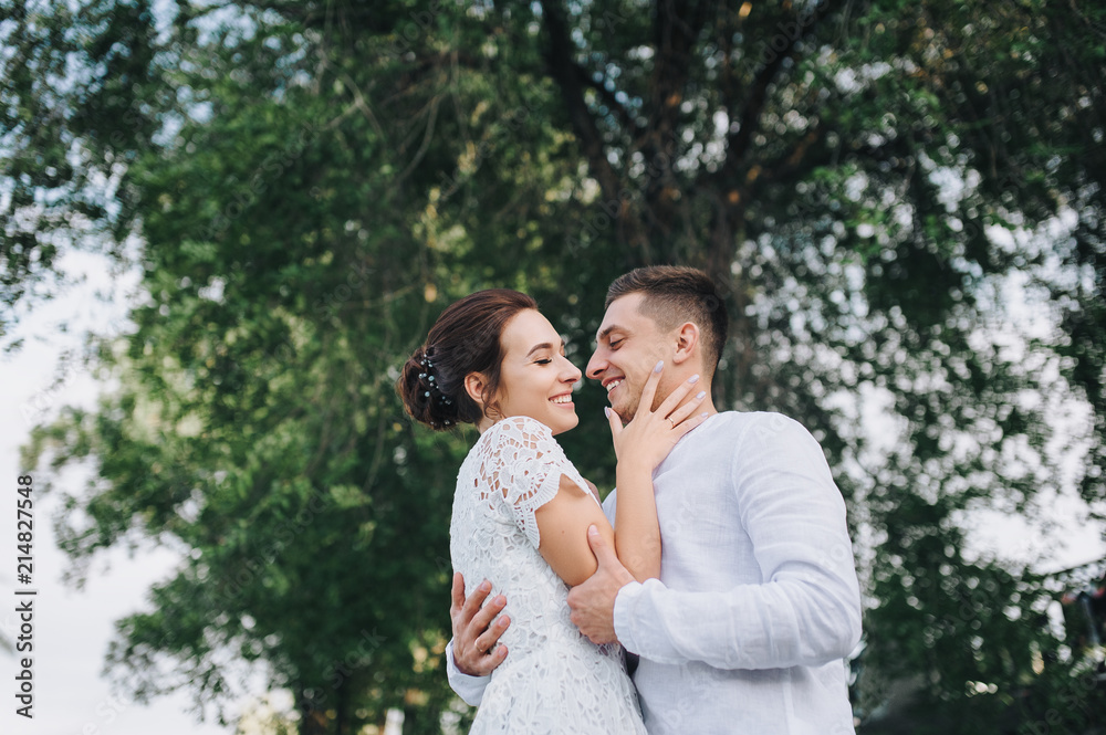 Beautiful newlyweds hugging against a background of green foliage. A stylish bridegroom gives love to a sweet bride. Wedding portrait. Beautiful newlyweds hugging against a background of green foliage. A stylish bridegroom gives love to a sweet bride. Wedding portrait.
