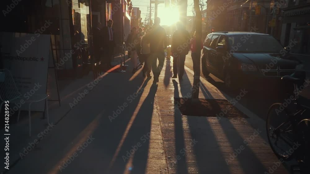 Beautiful evening sunlight shines into the lens as the camera passes through crowds of pedestrians in Toronto