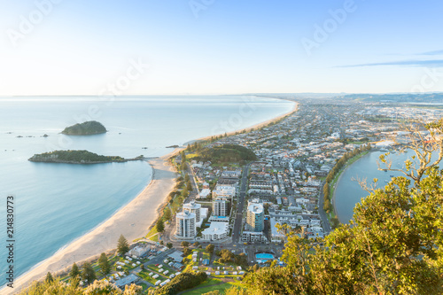 Mount Maunganui stretches out below as sun rises on horizon and falls across ocean beach and buildings