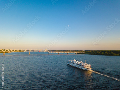 Aerial view white cruise ship on river Volga with railroad bridge on background. Cruise ship near Kostroma city at sunset.