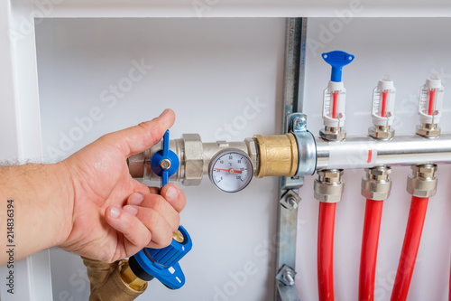 The man's hand closes the ball valve on the supply pipe of the collector for the warm floor