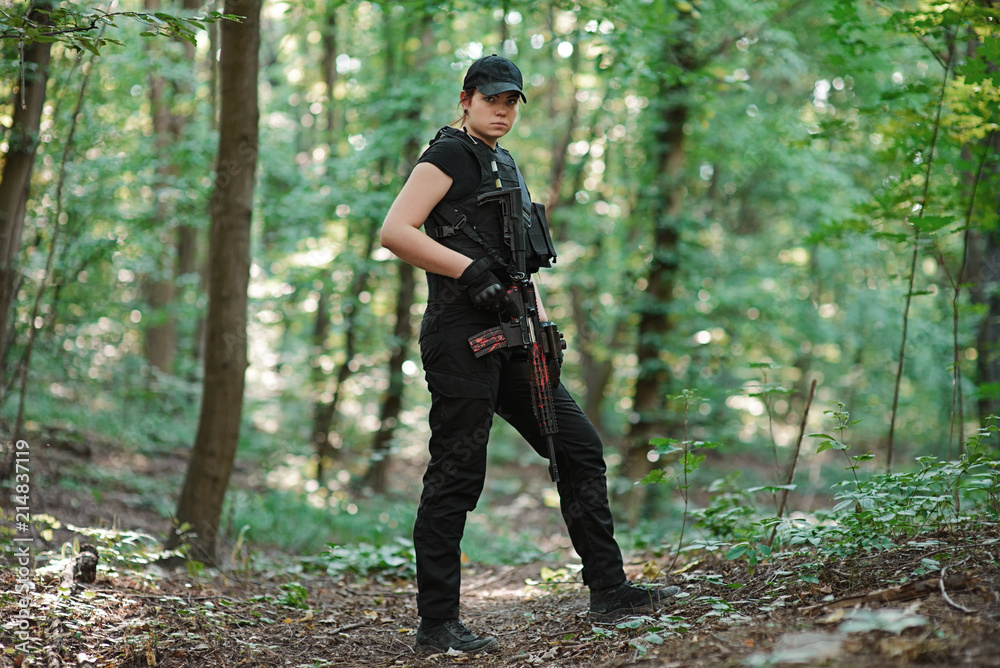 Woman with rifle in hands in black uniform in the forest.Selective focus