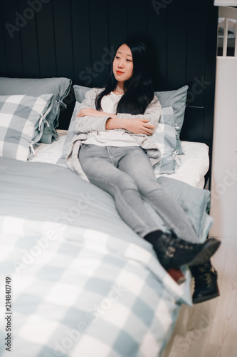 Full length portrait of beautiful young asian girl lying on a bed with light bed linen with white and blue check © mkphoto2000