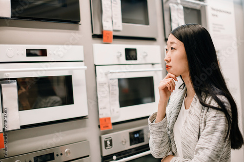 Close portrait of asian woman choosing new oven in furniture store