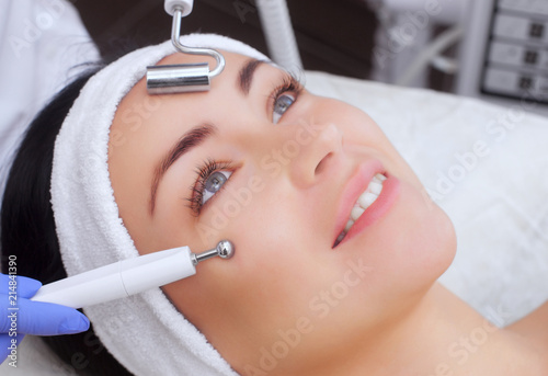 The cosmetologist makes the apparatus a procedure of Microcurrent therapy of a beautiful, young woman in a beauty salon. Cosmetology and professional skin care. photo