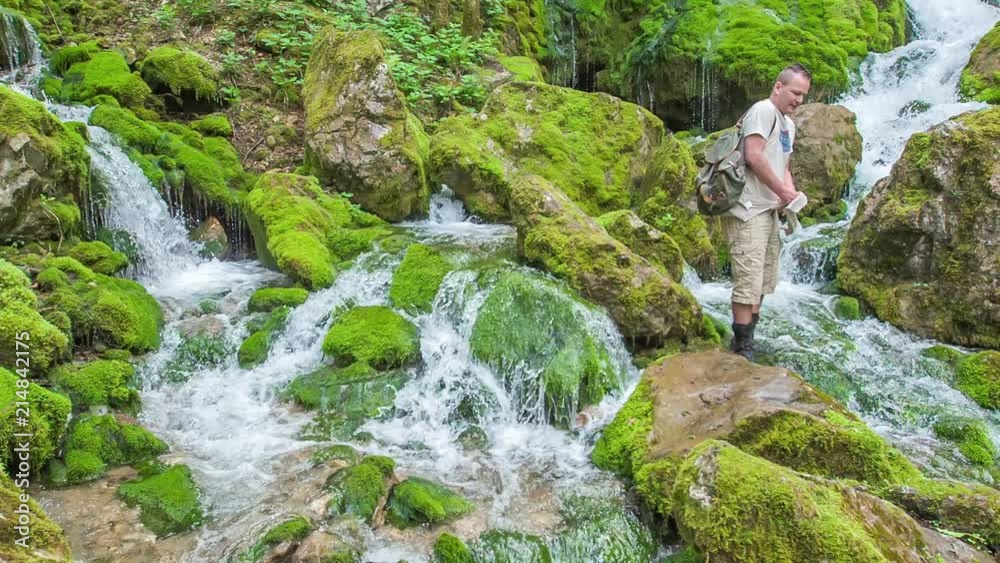 Water is flowing over the rocks covered with moss. A man is posing there so that someone will take a photo of him. Water is flowing over the rocks covered with moss. A man is posing there so that someone will take a photo of him.