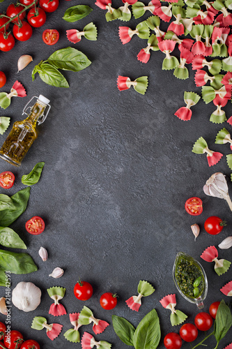 Pasta farfalle, cherry tomatoes, garlic, olive oil and basil on dark background with copy space