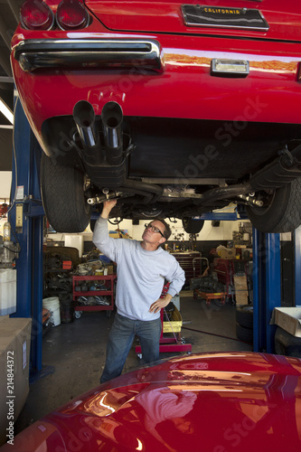 Owner of auto repair shop inspecting automobile elevated on a lift