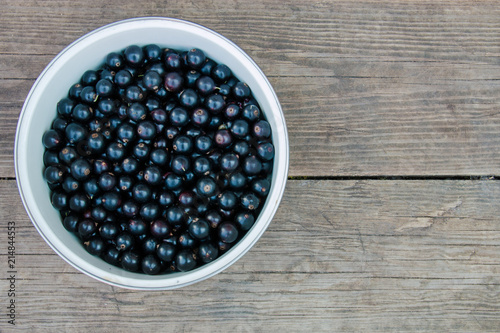 Beautiful natural black berries in a bowl on wooden background top view