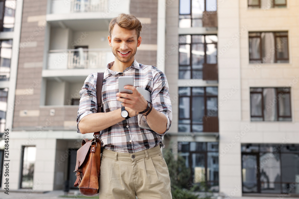 Digital media. Happy joyful man smiling while looking at his smartphone screen Digital media. Happy joyful man smiling while looking at his smartphone screen
