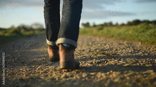 Man in hiking boots and jeans walking along a dirt path. Sunrise or sunset. photo