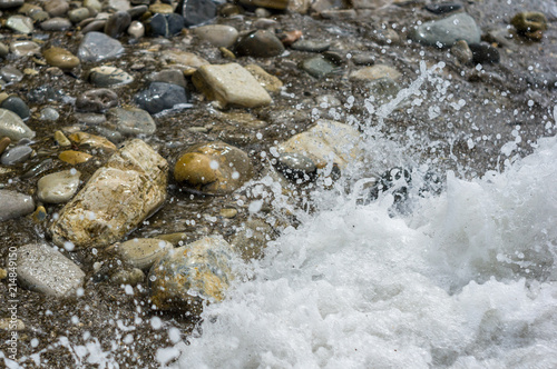 pebble stones on the sea beach, the rolling waves of the sea with foam