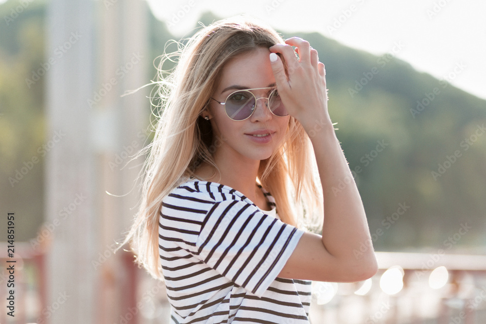 Outdoor portrait of blissful enjoyable slim model having fun alone in weekend. Photo of charming blonde lady wearing trendy striped attire and enjoying good warm day