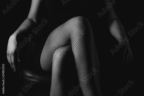 Girl in black fishnet stockings against dark background. Sexy woman in stockings sitting on chair. Strict woman domination bdsm concept.