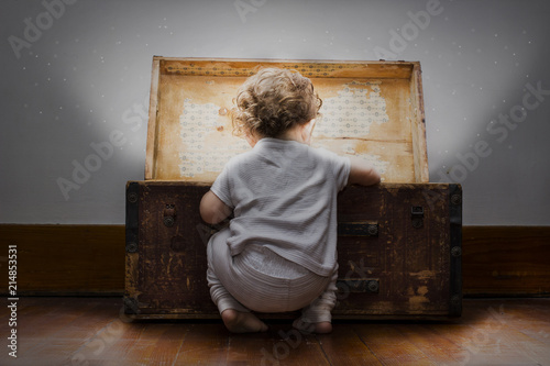 An adorable little child dressed in pajamas with diaper sticking out looks into a mysterious bright treasure chest. 