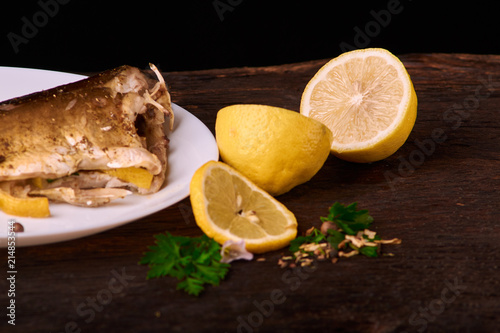 Appetizing baked fish, covered with juicy lemons, garlic and salt on side, above view