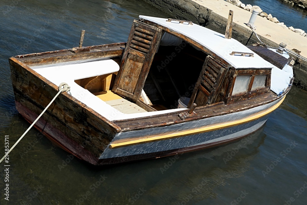 Older wooden fishing boat with peeling enamel paint and white roof, front  side and seats, tied to a concrete molo in Croatian marina Stock Photo