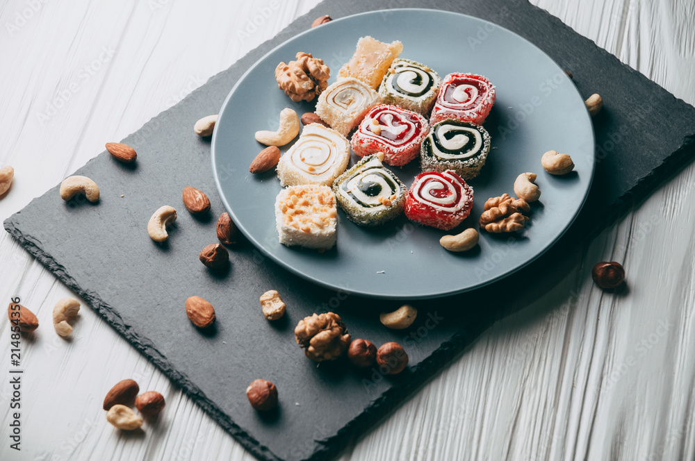 Traditional oriental sweets and nuts: hazelnuts, cashews on a white wooden background. Turkish dessert is the locus of Rahat. View from above. Place under the text. Traditional oriental sweets and nuts: hazelnuts, cashews on a white wooden background. Turkish dessert is the locus of Rahat. View from above. Place under the text.