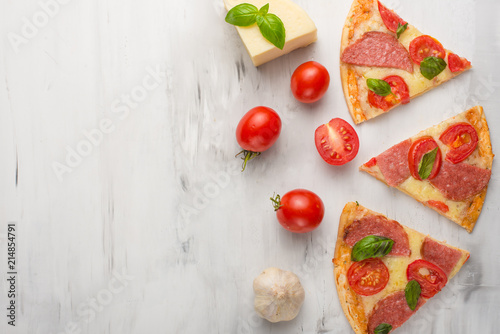 Delicious sliced pizza with tomatoes, mozzarella cheese, basil, and a tomato on a light background,Copyspace. Top view.