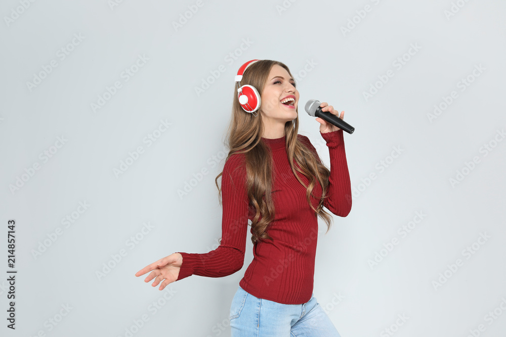 Obraz premium Young woman singing into microphone on color background. Christmas music