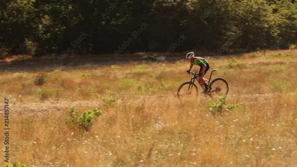 Teenage male mountain biking on a single track in a dry and brown dusty field on a summers day Teenage male mountain biking on a single track in a dry and brown dusty field on a summers day