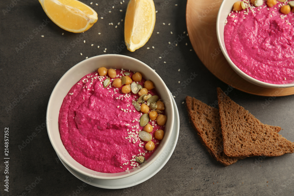 Flat lay composition with bowls of tasty beet hummus, slices of bread and lemon on dark background Flat lay composition with bowls of tasty beet hummus, slices of bread and lemon on dark background