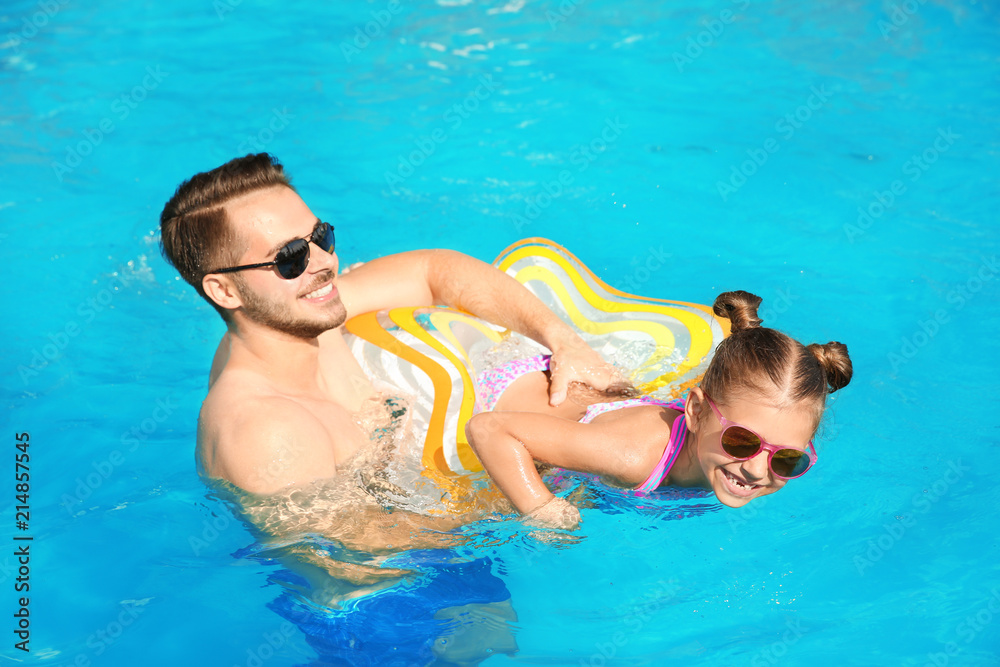 Father teaching daughter to swim with inflatable star in pool on sunny day
