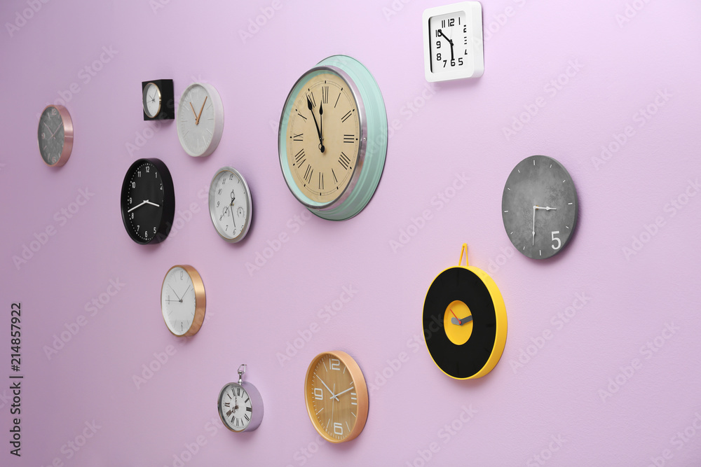 Many different clocks hanging on color wall. Time of day