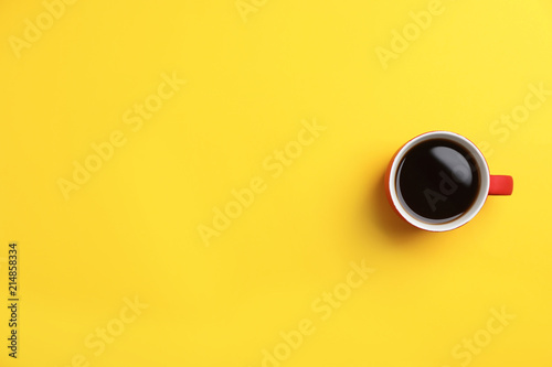 Ceramic cup with hot aromatic coffee on color background, top view